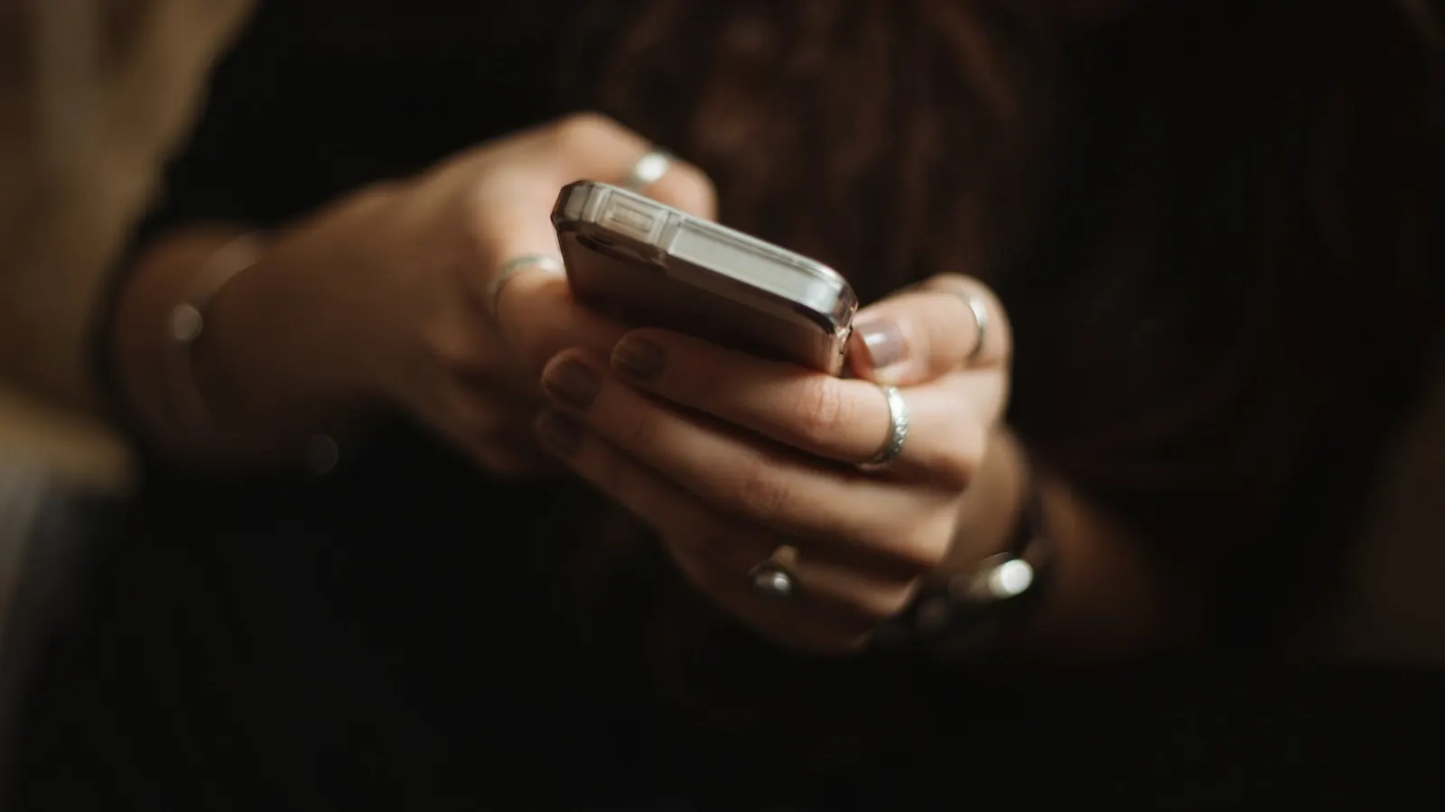 Mãos segurando um smartphone em um ambiente com pouca luz