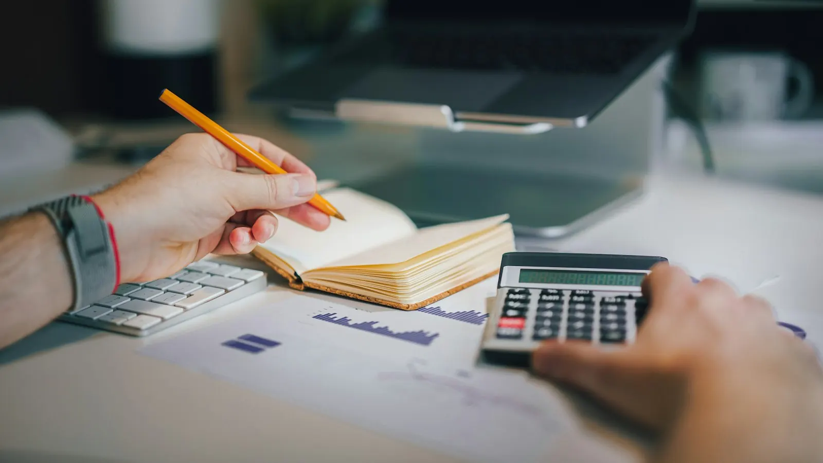 Pessoa fazendo contas com calculadora e caderno em uma mesa de trabalho